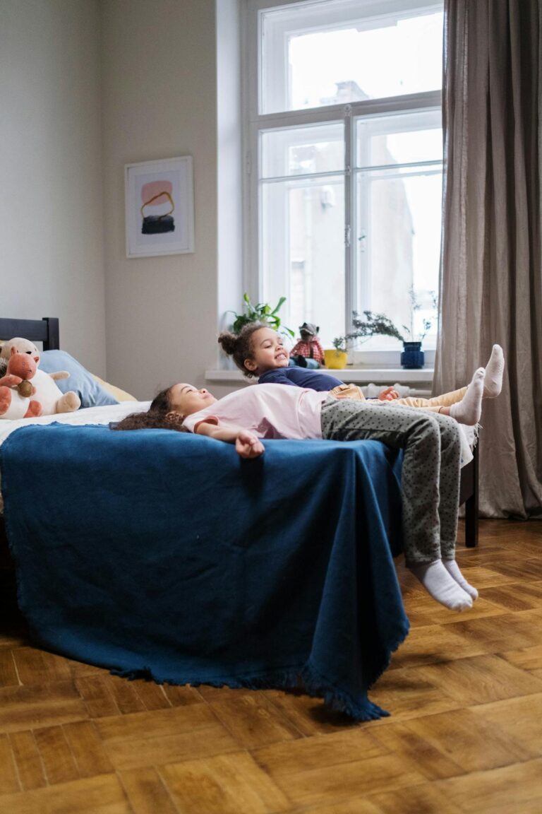 Two young girls relaxing together on a cozy bed in a bright, modern bedroom.